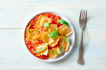 Ravioli with tomato sauce and fresh basil leaves on a plate, overhead flat lay shot on a rustic wooden background, with a fork