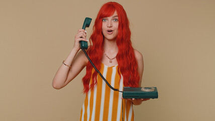 Hey you, call me back. Cheerful one ginger woman secretary in tank top talking on wired vintage telephone of 80s, says hey you call me back. Young redhead girl posing isolated on beige wall background