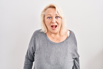 Middle age caucasian woman standing over white background afraid and shocked with surprise and amazed expression, fear and excited face.