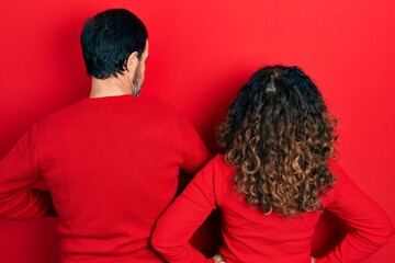 Middle age couple of hispanic woman and man hugging and standing together standing backwards looking away with arms on body
