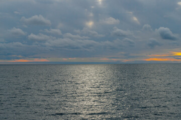 Obraz premium Calm sea and blue sky with white cirrus clouds. The sun shines through the clouds.
