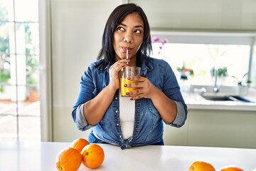 Hispanic brunette woman drinking a glass of fresh orange juice at the kitchen