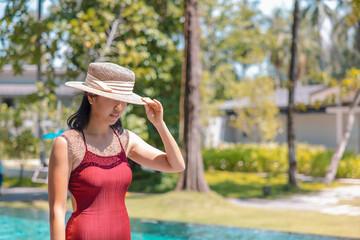 Happy asian woman in red swimsuit and a straw hat relaxing walk by the pool at Koh Mak, Phangnga, Thailand. relax and travel concept. Comfort resort summer vacation