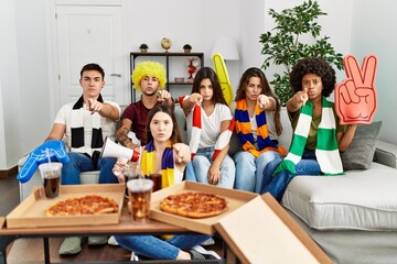 Group of young people wearing team scarf cheering football game pointing with finger to the camera and to you, confident gesture looking serious