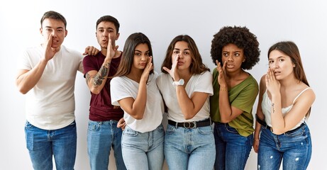 Fototapeta premium Group of young friends standing together over isolated background hand on mouth telling secret rumor, whispering malicious talk conversation