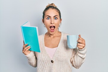 Beautiful caucasian woman with blond hair reading a book and drinking a cup of coffee celebrating crazy and amazed for success with open eyes screaming excited.