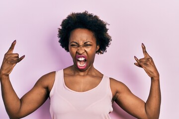 Young african american woman wearing casual sleeveless t shirt shouting with crazy expression doing rock symbol with hands up. music star. heavy concept.