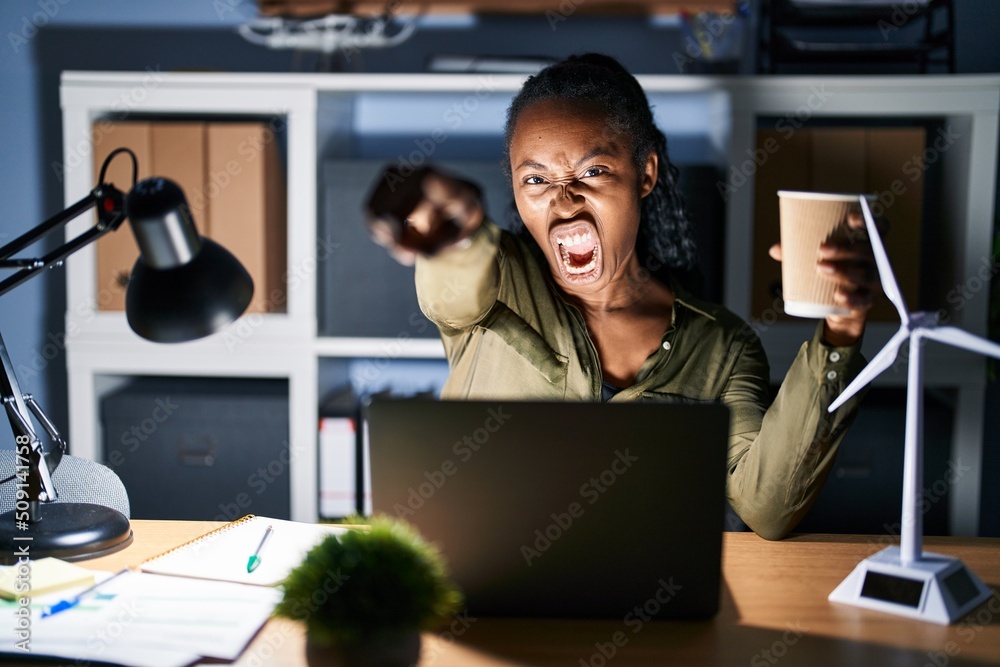 Sticker african woman working using computer laptop at night pointing displeased and frustrated to the camer