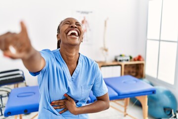 Obraz premium Black woman with braids working at pain recovery clinic laughing at you, pointing finger to the camera with hand over body, shame expression