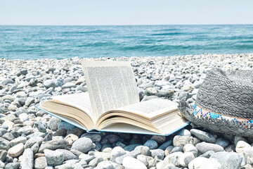 Open book and male straw hat on the pebble beach. Concept of reading and relaxing in summer...