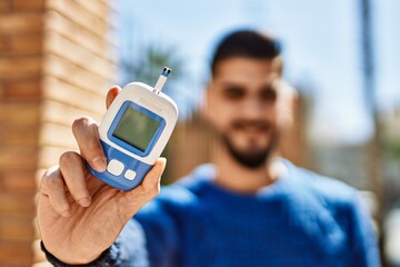 Young arab man smiling confident holding glucometer at street