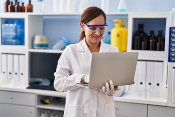 Obraz na płótnie Canvas Middle age woman wearing scientist uniform using laptop at laboratory