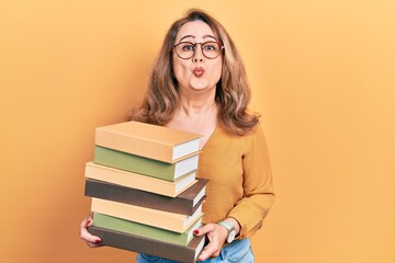 Middle age caucasian woman holding a pile of books looking at the camera blowing a kiss being lovely and sexy. love expression.