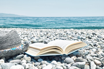 Open book and male straw hat on the pebble beach. Concept of reading and relaxing in summer...
