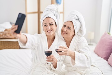 Mother and daughter make selfie by the smartphone drinking glass of wine at bedroom
