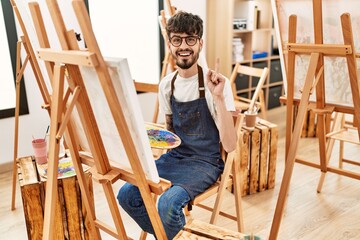 Hispanic man with beard at art studio surprised with an idea or question pointing finger with happy face, number one