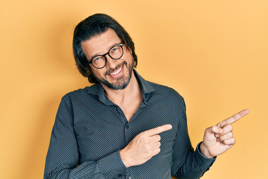 Middle age caucasian man wearing casual clothes and glasses smiling and looking at the camera pointing with two hands and fingers to the side.