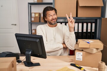 Handsome middle age man working at small business ecommerce smiling with happy face winking at the camera doing victory sign. number two.