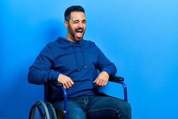 Handsome hispanic man with beard sitting on wheelchair winking looking at the camera with sexy...