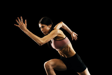 Studio shot of young muscular woman running isolated on black background. Sport, track-and-field...