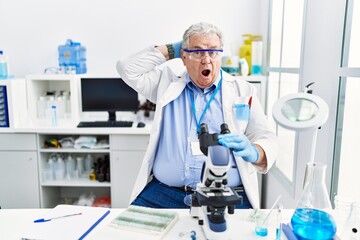 Senior caucasian man working at scientist laboratory crazy and scared with hands on head, afraid and surprised of shock with open mouth