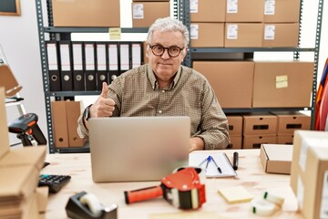 Senior caucasian man working at small business ecommerce with laptop doing happy thumbs up gesture with hand. approving expression looking at the camera showing success.