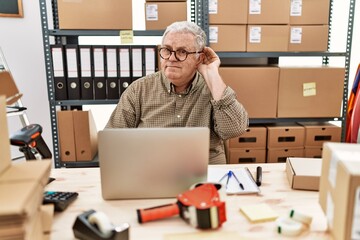 Senior caucasian man working at small business ecommerce with laptop smiling with hand over ear listening an hearing to rumor or gossip. deafness concept.