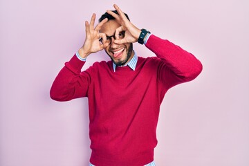 Hispanic man with beard wearing business shirt and glasses doing ok gesture like binoculars sticking tongue out, eyes looking through fingers. crazy expression.