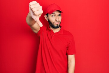 Hispanic man with beard wearing delivery uniform and cap looking unhappy and angry showing rejection and negative with thumbs down gesture. bad expression.
