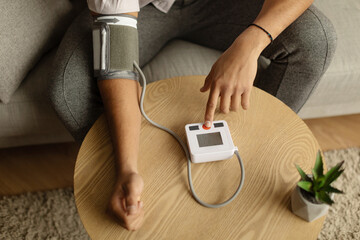 Top view of unrecognizable black male patient using modern tonometer at home, closeup