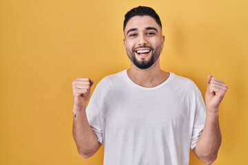 Young handsome man wearing casual t shirt over yellow background celebrating surprised and amazed for success with arms raised and open eyes. winner concept.