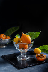 Yellow and orange Medlar fruits in glass cup over dark grey background. Chiaroscuro mood photo