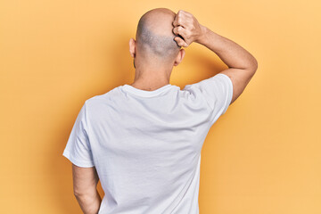 Young bald man wearing casual white t shirt backwards thinking about doubt with hand on head