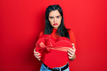 Young hispanic girl holding valentine gift skeptic and nervous, frowning upset because of problem. negative person.