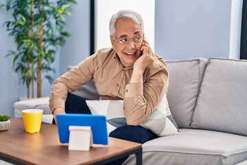 Senior man talking on the smartphone watching touchpad at home