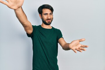 Fototapeta premium Young hispanic man wearing casual white tshirt looking at the camera smiling with open arms for hug. cheerful expression embracing happiness.