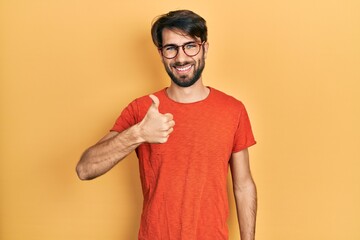 Young hispanic man wearing casual clothes and glasses doing happy thumbs up gesture with hand. approving expression looking at the camera showing success.