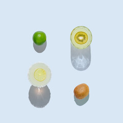 Minimal sunny scene with beverage in crystal cocktail glasses and sliced kiwi and lime on bright blue grey background. Square crop.