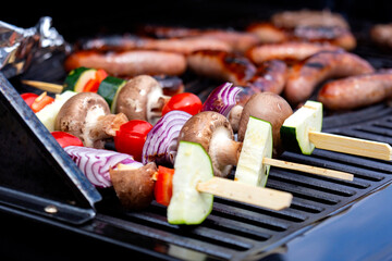 Vegetable kebabs, with courgette, red onion, red pepper, mushroom and tomato, cooking on a gas barbecue.