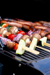 Vegetable kebabs, with courgette, red onion, red pepper, mushroom and tomato, cooking on a gas barbecue.