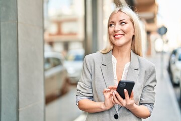 Young blonde woman smiling confident using smartphone at street