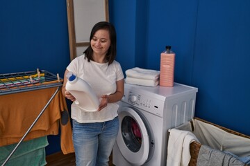 Down syndrome woman smiling confident holding detergent bottle at laundry room