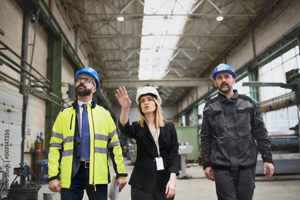 Wall mural Manager supervisors and industrial worker in uniform walking in large metal factory hall and talking. - Wall murals