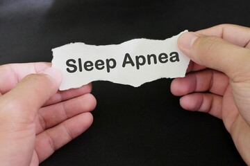 Sleep Apnea sleeping disorder diagnosis concept. Hand holding paper with written word text in black background.