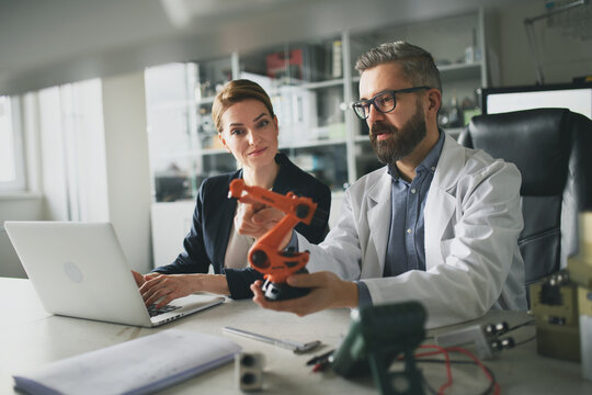 Robotics engineers working on laptop and desinging modern robotic arm in laboratory.