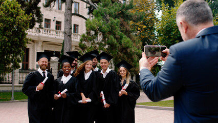 Happy and excited group of multiracial graduates students posing in front of a smartphone one of...