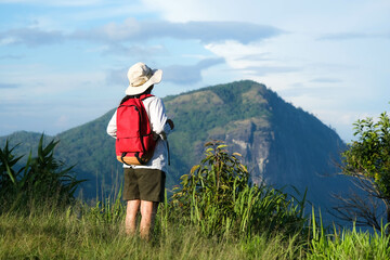 Happy female hiker with a backpack stands on top of a mountain enjoying nature and looking at the sky. Freedom and happiness, achievement in mountains.