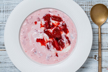 White plate with red strawberries and natural yogurt on a wooden table, top view