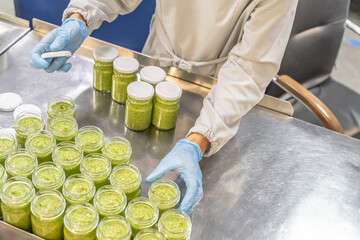 Pesto sauce Industrial process. worker tightens the lids on jars of pesto. production of Pesto...