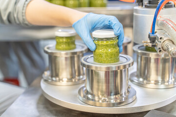 Pesto sauce Industrial process. High quality sauce production. Factory worker working on vacuum sealing machine for canned food. Italian basil taste in Pesto sauce. Vacuum Seamer for Cylindrical Cans